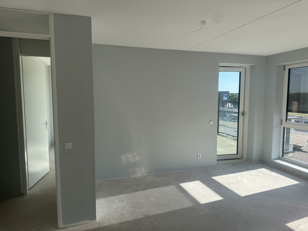 Nieuwbouwappartement met pas gesausde lichtgrijze wanden, een balkondeur en een kale betonvloer