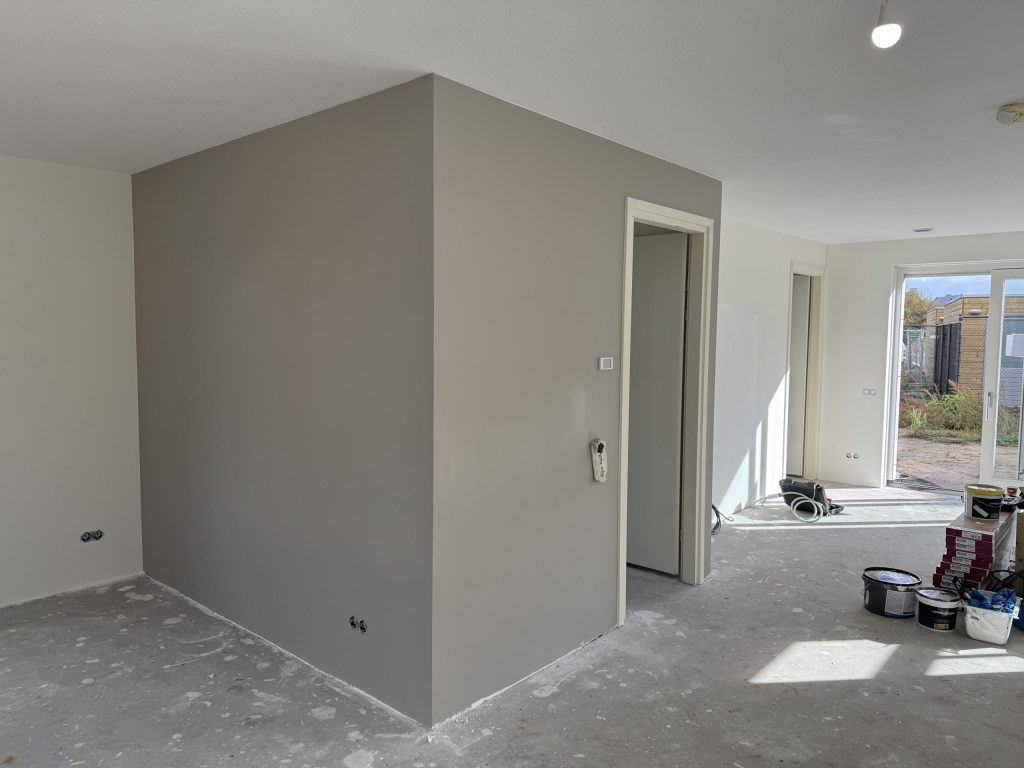 Nieuwbouwwoonkamer met een pas geverfde grijze wand, verfemmers en een kale betonvloer